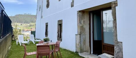 A white building with a patio area featuring a table and chairs, a view of the surrounding landscape, and a door leading to an interior space.