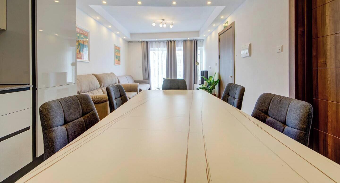 A conference room with a long table, four chairs, a sofa, and a plant.