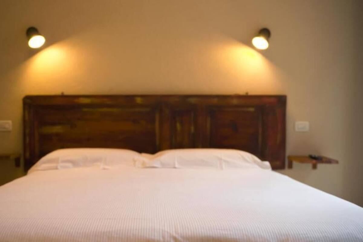 Una cama con cabecera de madera, dos mesitas de noche y luces fijadas a la pared.