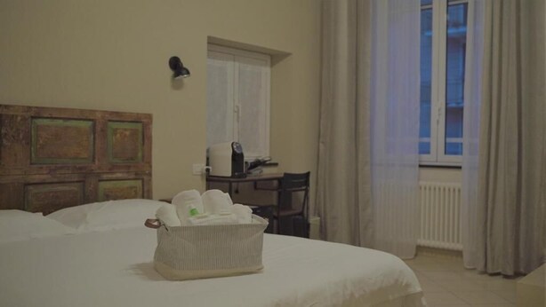 A hotel room with a bed, a bedside table, a chair, a window with curtains, and a wall-mounted lamp. - Piccolo Borgo (Chiavari)