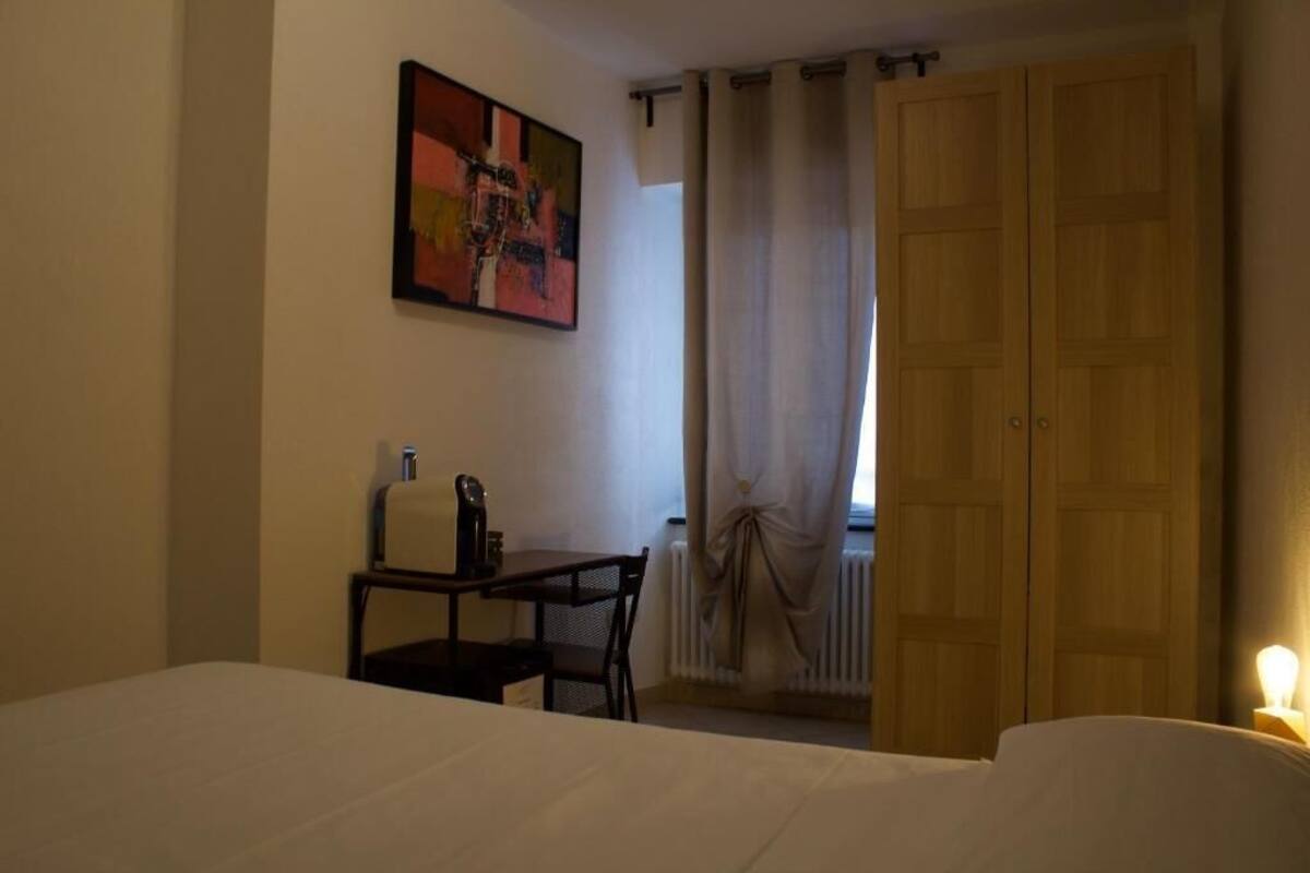 Una habitación de hotel con una cama, un escritorio con una silla, un radiador y una puerta.