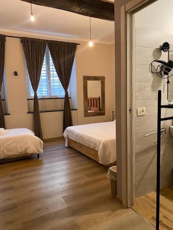 A bedroom with two beds, a mirror, a wooden floor, and a door leading to a bathroom.