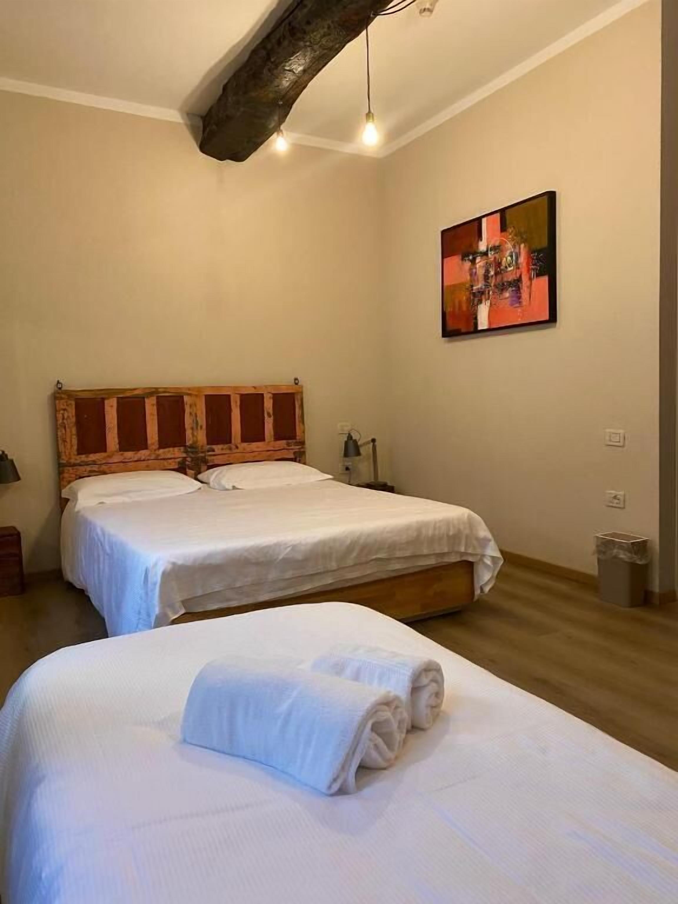 A bedroom with two beds, a wooden headboard, a painting on the wall, and a hanging light fixture.