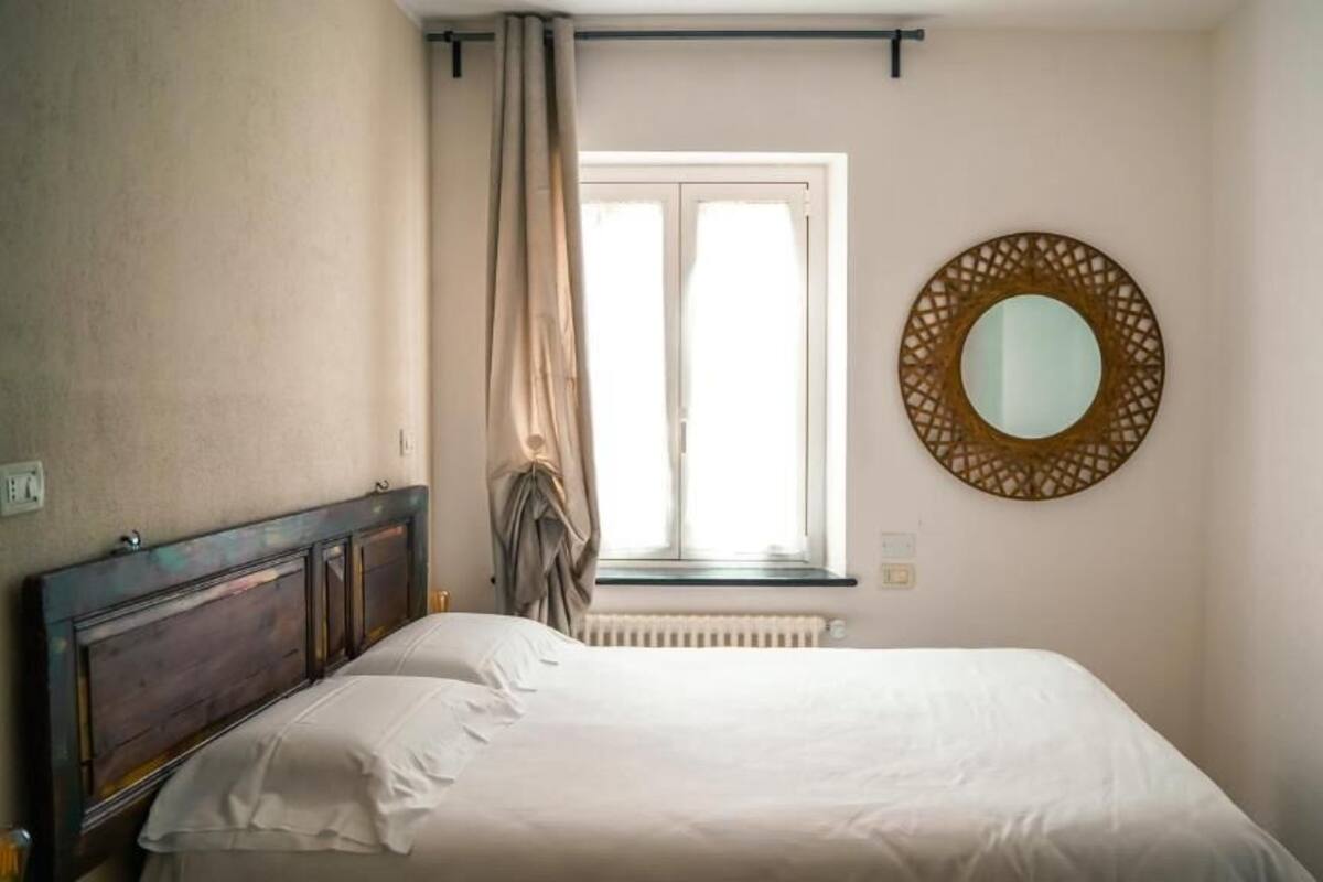 Un dormitorio con cama, ventana con cortinas, radiador y un espejo redondo en la pared.