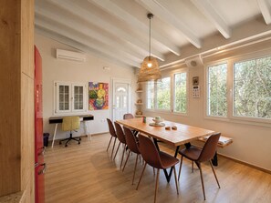 A dining area with a wooden table, chairs, a hanging light fixture, and large windows with a view of trees. - Virginia's Penthouse (Corfu)
