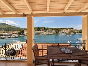 A wooden table and chairs on a balcony with a view of a marina and buildings. - Virginia's Penthouse (Corfu)