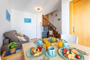 A dining area with a table set for breakfast, a sofa, a staircase, and a door. - Bright apartment in Aloha playa (Benalmádena)