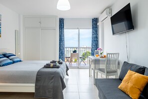 A hotel room with a bed, a sofa, a TV, a balcony with a table and chairs, and a view of the city. - ANDREA 2 - Modern studio apartment with beautiful view in Ju (Arroyo de la Miel)