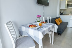 A dining area with a table set for two, a potted plant, and a TV mounted on the wall. - ANDREA 2 - Modern studio apartment with beautiful view in Ju (Arroyo de la Miel)