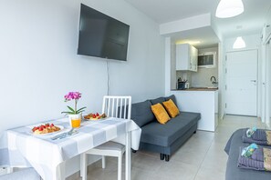 A modern living room with a flat-screen TV, a dining table with breakfast, a gray sofa, and a kitchen area. - ANDREA 2 - Modern studio apartment with beautiful view in Ju (Arroyo de la Miel)