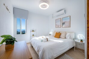 A bedroom with a bed, bedside tables, a window with a view, and an air conditioning unit. - NICOLE - Flat in Iris with beautiful views (Arroyo de la Miel)