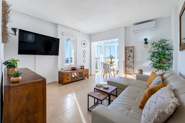 A modern living room with a flat-screen TV, a wooden cabinet, a sofa, a coffee table, and a dining area with chairs and a table. - NICOLE - Flat in Iris with beautiful views (Arroyo de la Miel)