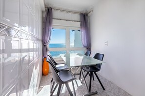 A room with a glass table, four chairs, a large orange vase, and a view of the sea through a window with purple curtains. - Cozy apartment for 5 in front of the sea (Benalmádena)