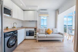 A modern kitchen with a built-in oven, a washing machine, and a dining area with a sofa and a balcony with a city view. - Renovated apartment with beautiful views in Iris (Benalmádena)