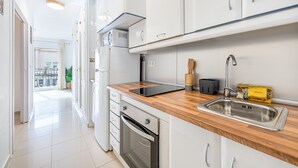 Une cuisine moderne avec des armoires blanches, un plan de travail en bois, un four encastré et un évier en acier inoxydable.