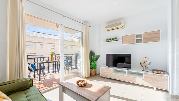Un salon moderne avec un téléviseur, une table basse en bois, un canapé et un balcon offrant une vue sur les immeubles.