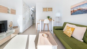 Un salon moderne avec un téléviseur, un canapé vert, une table basse et un coin cuisine à l’arrière-plan.