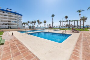 A swimming pool with two separate sections, surrounded by palm trees and a clear sky. - Cozy studio in Aloha (Benalmádena)