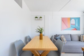 Un salon moderne avec une table à manger en bois, un canapé gris et un tableau abstrait aux couleurs vives.