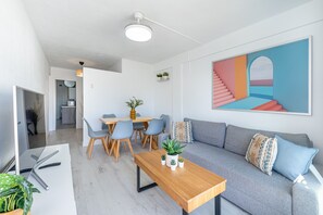 Un salon moderne avec un canapé, une table à manger et des chaises. Un tableau orne le mur et un luminaire est suspendu au plafond.