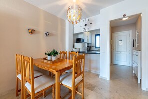 A dining area with a wooden table and chairs, a chandelier, and a kitchen in the background. - Cozy apartment for 5 in Torrequebrada (Benalmádena)