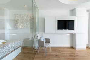 Ein modernes Schlafzimmer mit einem Bett, einem Sessel, einem an der Wand montierten Fernseher und einer Wanddekoration.