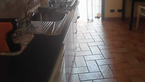 Uma cozinha com painel de azulejos, pia e fogão. Há uma porta que dá para outro cômodo.
