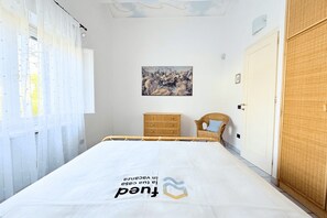 Une chambre à coucher avec un lit, un tableau au mur, une chaise en osier et une armoire.