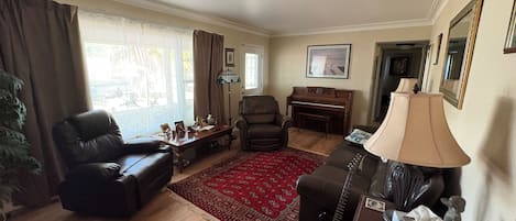 Una sala de estar con un piano, sillones de cuero, un tapete rojo y una lámpara.