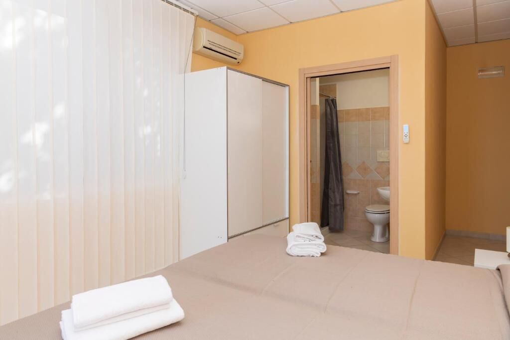 A hotel room with a bed, a wardrobe, an air conditioning unit, a bathroom with a toilet and shower curtain.