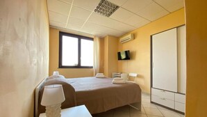 Een hotelkamer met een bed, een nachtkastje met een lamp, een aan de muur bevestigde televisie en een kledingkast.