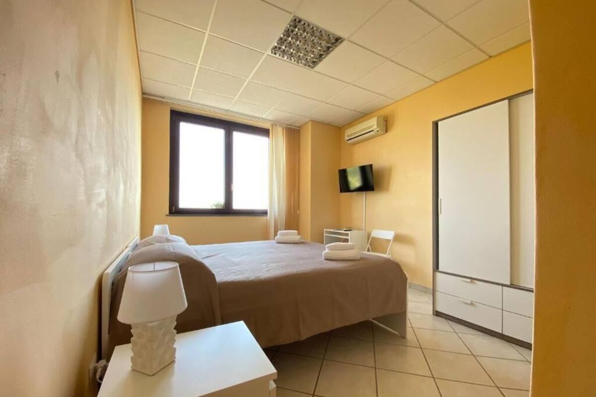 Una camera d'albergo con un letto, un comodino con una lampada, una TV a parete e un armadio.