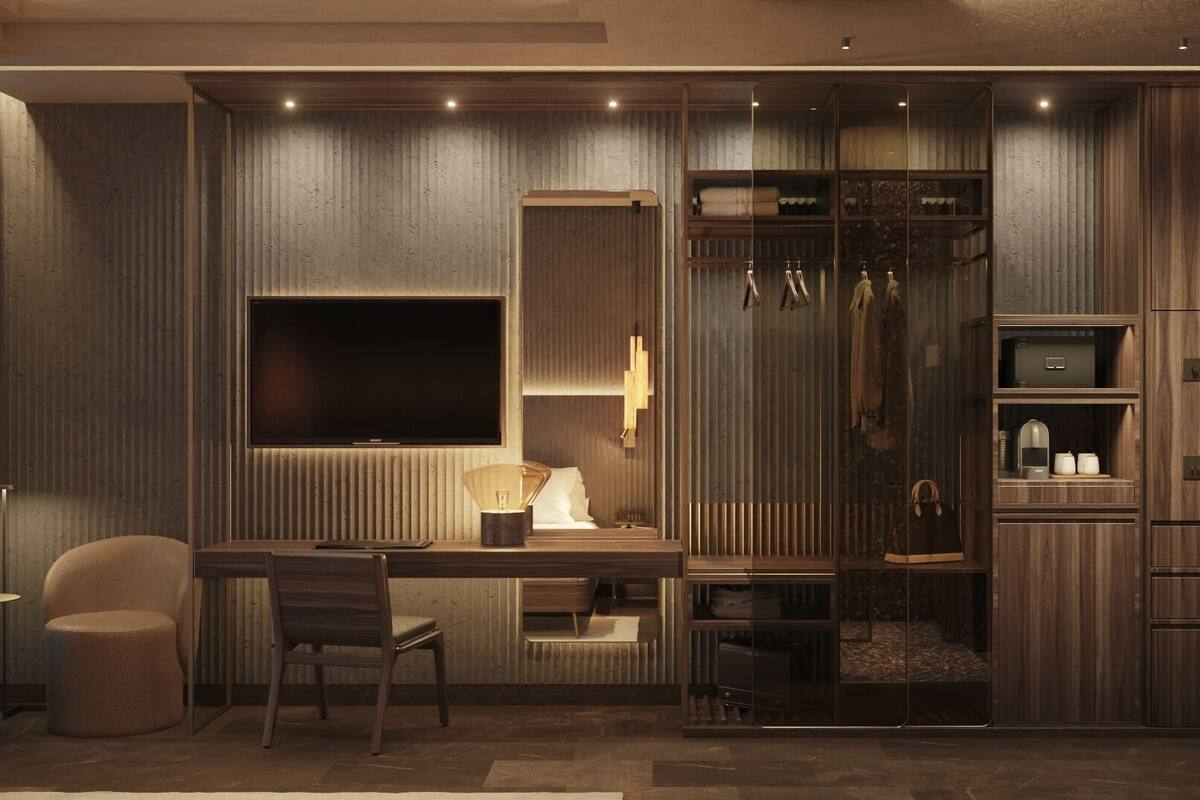 Une chambre d’hôtel moderne, dotée d’un bureau en bois, d’une chaise, d’une télévision et d’une armoire intégrée avec des étagères et des crochets.
