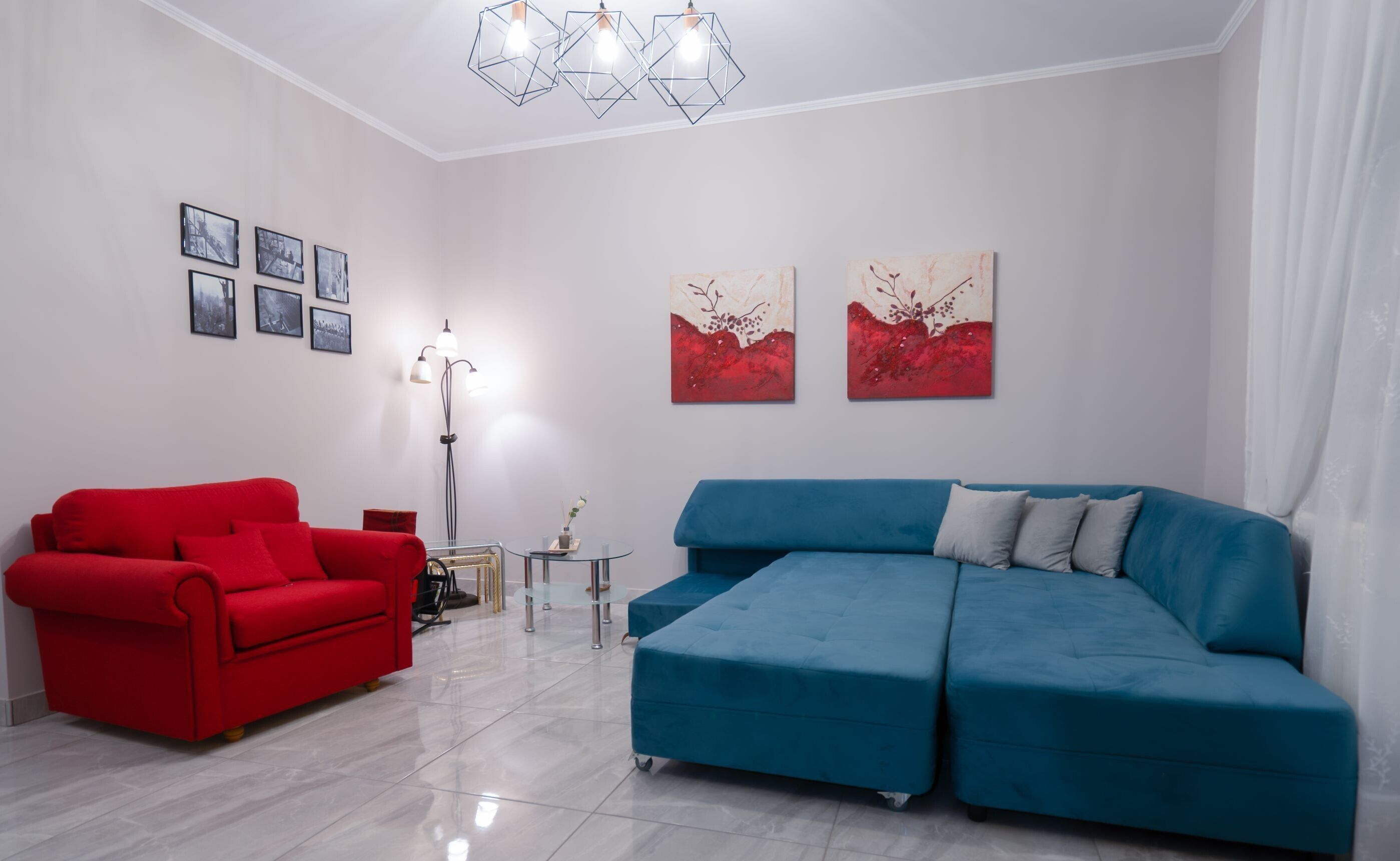 Un salon moderne avec un canapé rouge, un canapé d’angle bleu et des œuvres d’art abstraites accrochées aux murs.
