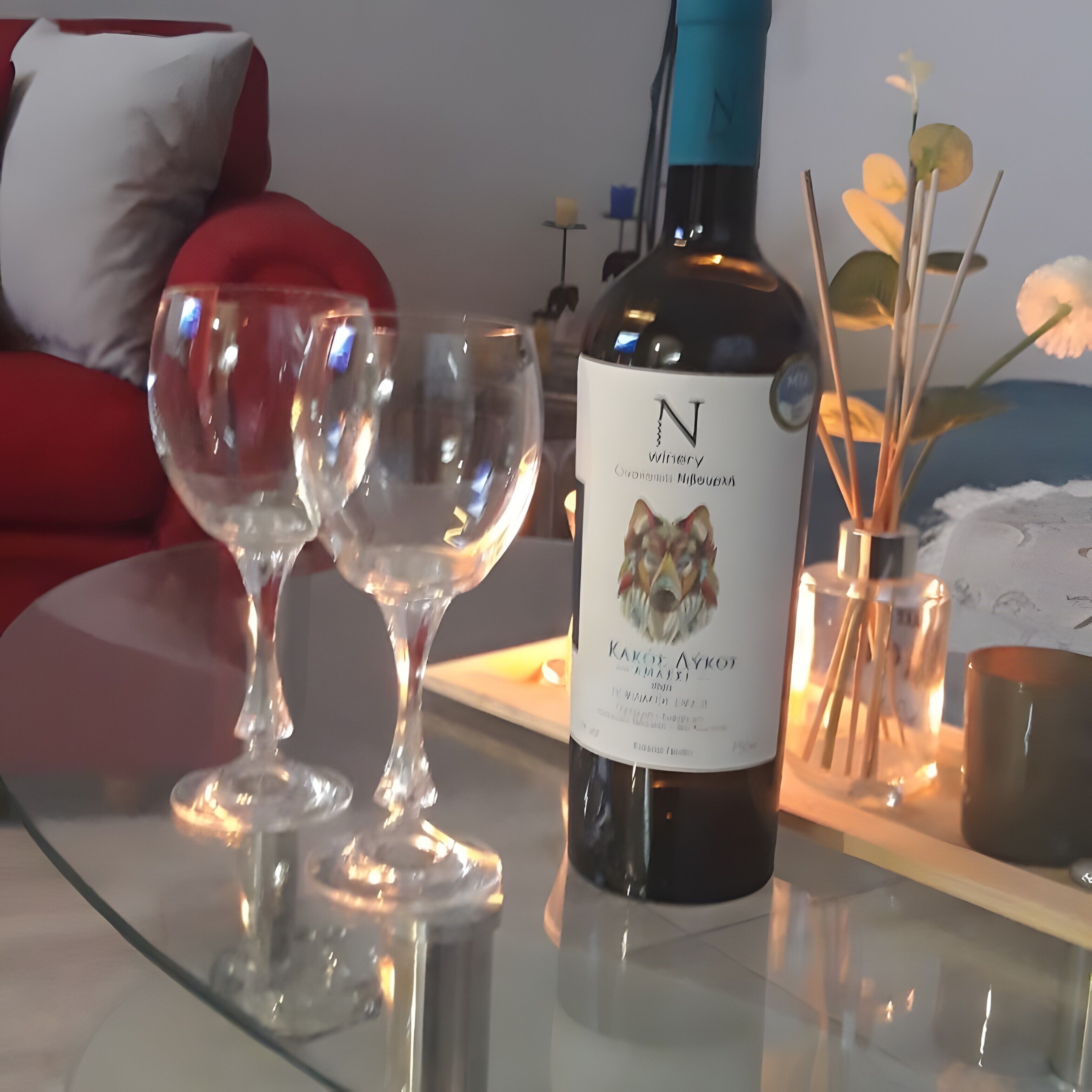 A bottle of wine with a label, two empty wine glasses, and a candle holder with a candle on a table.