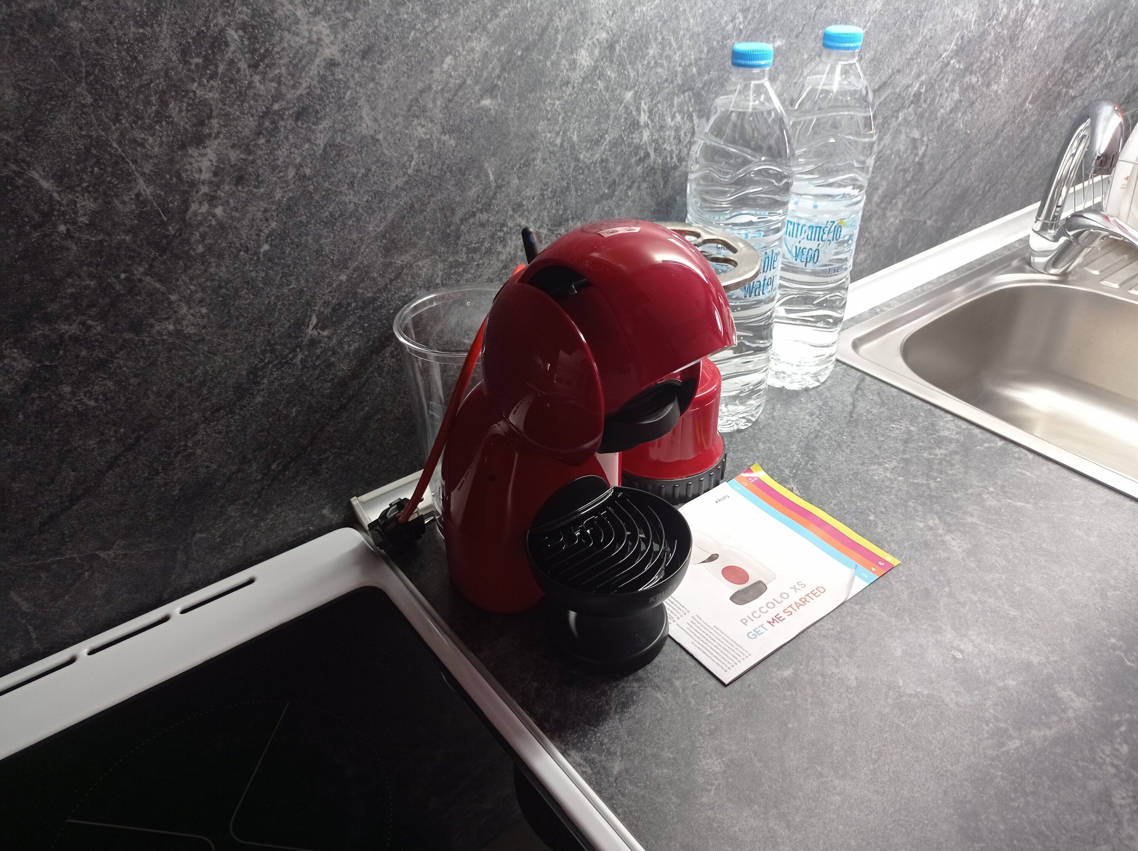 A kitchen with a red appliance, two water bottles, a glass, and a booklet on the counter.
