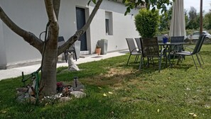En patio med bord og stole, et lille træ og en bygning med dør og vindue.