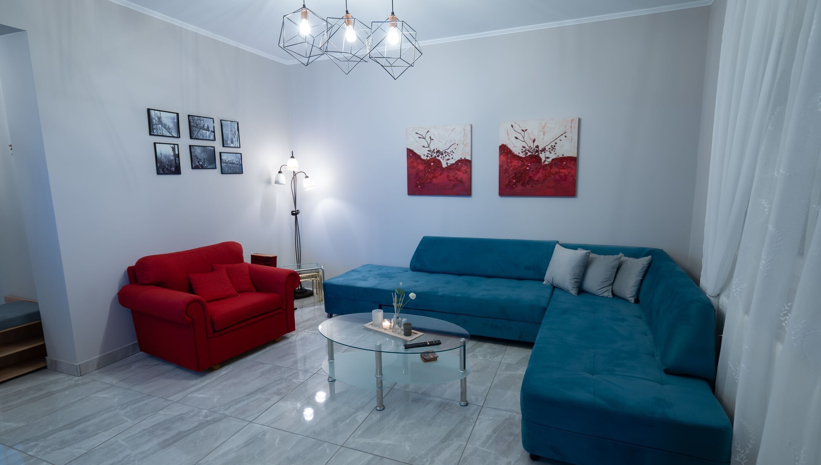 A modern living room with a red sofa, a blue sofa, a glass coffee table, and a floor lamp.
