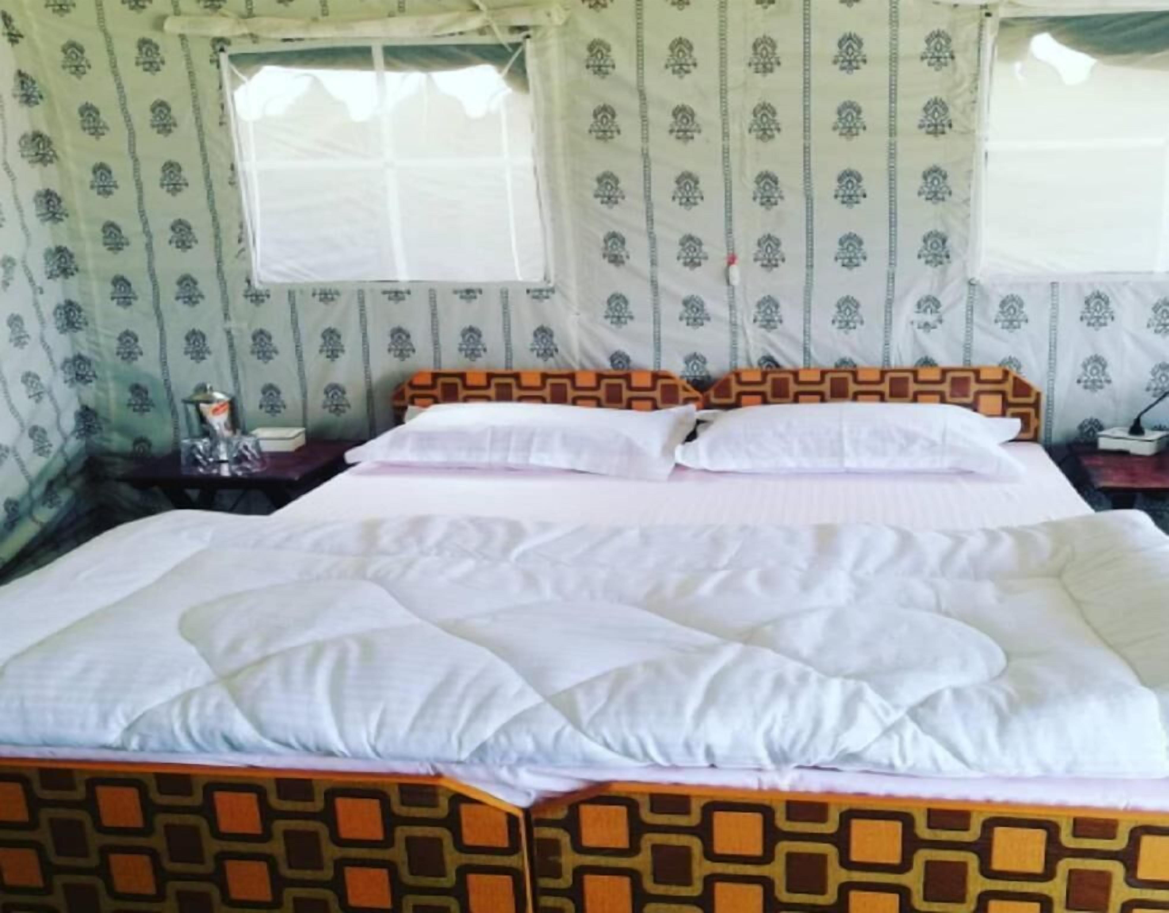A bed with a patterned headboard, a bedside table with a lamp, and a window with a curtain.