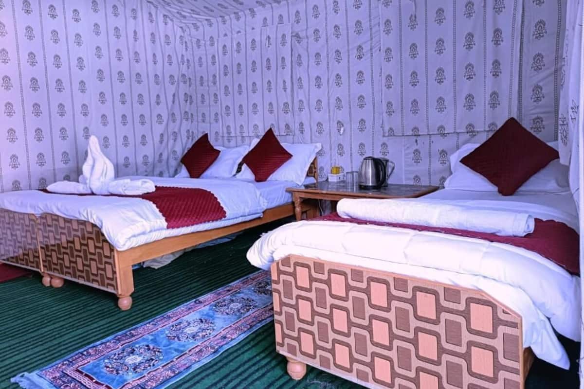 Ein Zimmer mit zwei Holzbetten, weißer Bettwäsche, roten Kissen, einem kleinen Tisch mit Wasserkocher und Wandverkleidungen mit Muster.