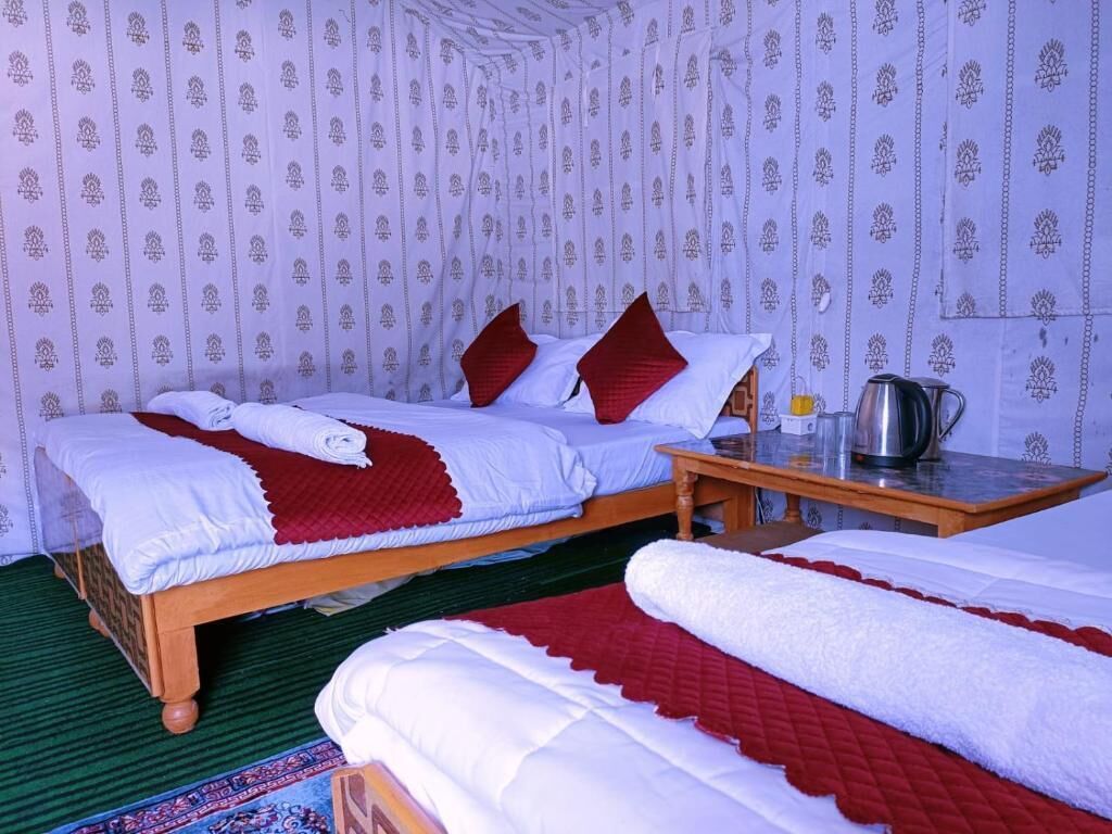 A room with two beds, a wooden table, and a patterned wall.