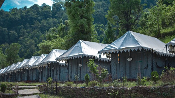 A row of tents with a stone wall in front, set in a grassy area with trees in the background. - Kedarnath Eco Resort  (Ukhimath)