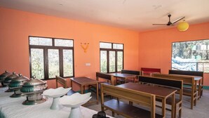 A classroom with wooden desks and benches, large windows, and a ceiling fan. - Kedarnath Eco Resort  (Ukhimath)