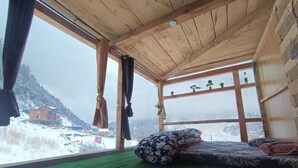 Ett rum med ett stort fönster, en säng med mönstrat sänglinne och utsikt över ett snötäckt landskap.