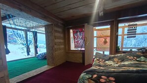 En stuga med träpanel, ett sovrum med en säng, ett fönster med utsikt över ett snötäckt landskap och en dörr som leder ut till ett område utomhus.