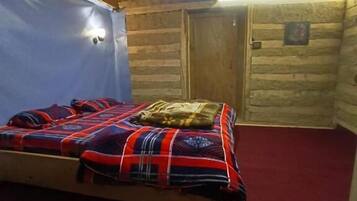 Un dormitorio tipo cabaña de madera con una cama, una puerta de madera y una pequeña lámpara en la pared.
