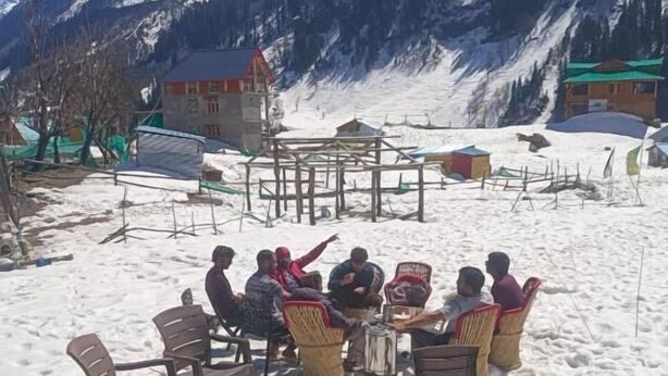 En grupp människor sitter utomhus på en snötäckt plats med berg i bakgrunden.