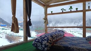 Ett rum med en säng, utsikt över ett snötäckt landskap och ett fönster med gardiner.