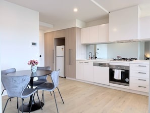 A modern kitchen with white cabinets, a built-in oven, and a dining area with a table and chairs. - Resort Living at M-City, 2BR 2BA w Parking&Balcony (Clayton)