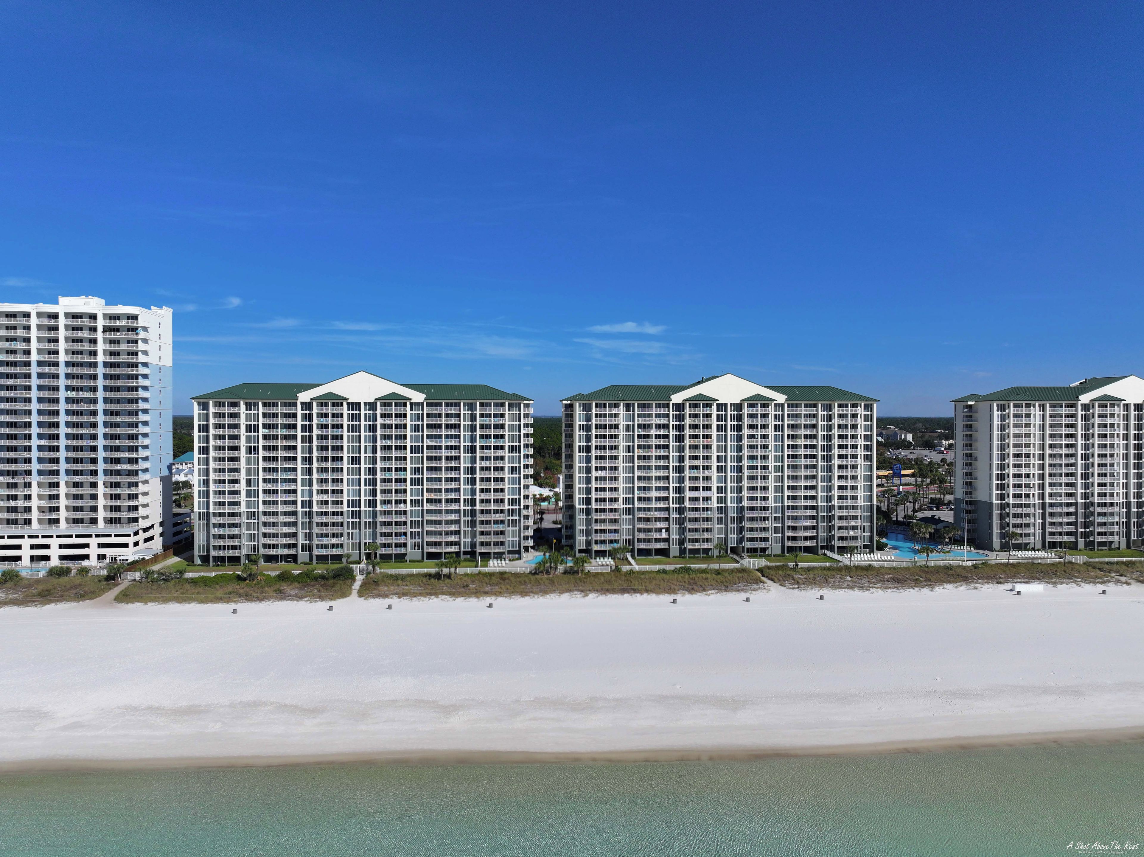 Un hôtel situé en bord de mer, composé de plusieurs immeubles de grande hauteur, avec une plage de sable fin et un ciel d’un bleu éclatant.